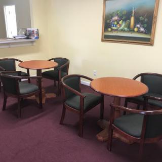 A cozy waiting area featuring two round tables and comfortable chairs, complemented by a decorative painting.