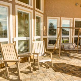 A sunny patio with rocking chairs and a swing, surrounded by large windows.