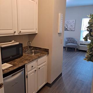 Small kitchen area with a microwave, mini fridge, and sink leading into a living space.