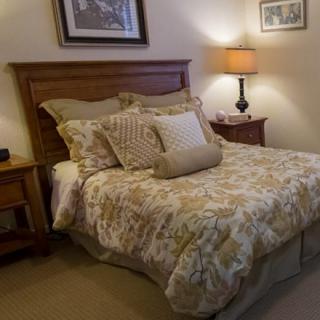 A cozy bedroom with a neatly made bed, warm lighting, and decorative pillows.