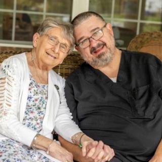 An elderly woman and a man sitting together, smiling and holding hands.