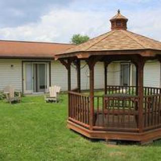 A wooden gazebo sits on a grassy lawn near a house.