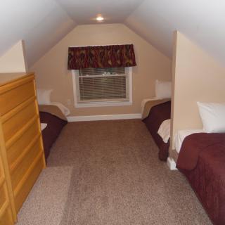 A small attic bedroom with two twin beds and a window with drapes.