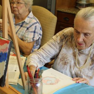 Two elderly women engaging in a painting activity indoors.