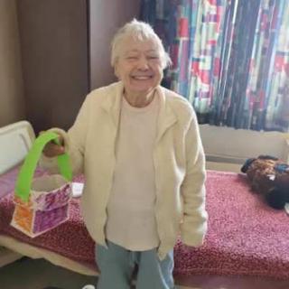 A cheerful elderly woman holding a colorful tote bag in her room.