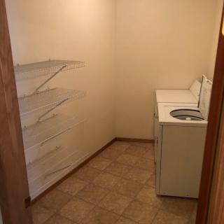 A small laundry room with a washer and dryer, featuring open shelves and a tiled floor.