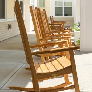 A row of wooden rocking chairs on a sunny porch.
