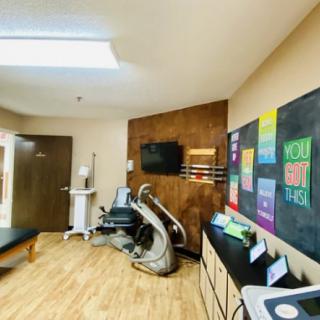 A modern chiropractic clinic treatment room with various therapy equipment and motivational posters on the walls.