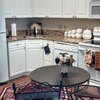 A modern kitchen with white cabinets, appliances, and a round table on a tiled floor.