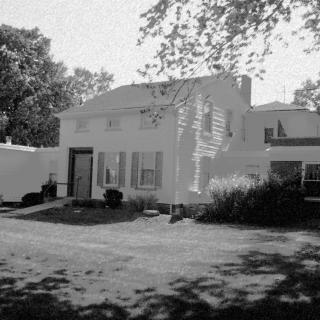 A black and white image of a suburban house surrounded by trees and a yard.