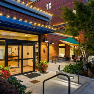 A well-lit building entrance with outdoor seating and decorative plants at night.