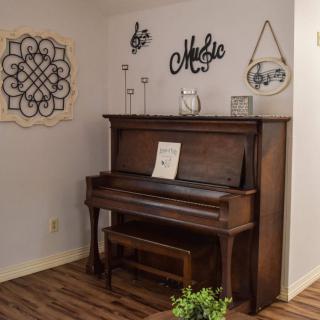 A cozy living room corner featuring a classic upright piano with decorative wall art and sheet music.