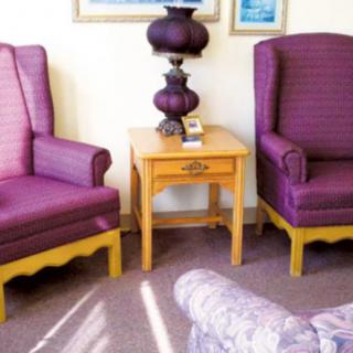 A cozy living room setup featuring two purple armchairs flanking a small wooden table with a decorative lamp.