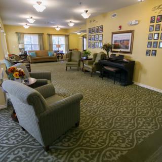 A cozy living room with comfortable seating and a piano, well-lit and decorated with photos on the walls.
