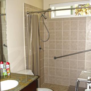 A bathroom featuring a tiled shower area with a curtain, a sink with a mirror above, and various toiletries.