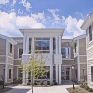 A modern residential building with a bright exterior and large windows, set against a blue sky.