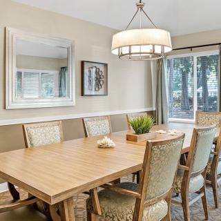 A modern dining room with a wooden table, upholstered chairs, and a chandelier above.