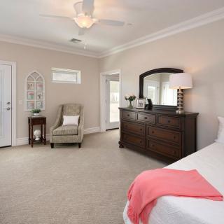 A spacious and elegantly decorated bedroom featuring a large dresser with a mirror, an armchair, and soft lighting.