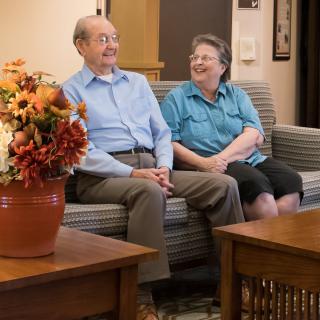 An elderly couple sitting and laughing together in a cozy living room.