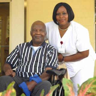 A caregiver and an elderly man share a moment outdoors.