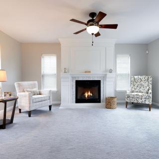 A cozy living room with a fireplace, armchairs, and ceiling fan.