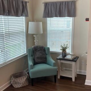 A cozy corner with a teal chair, white lamp, and side table by the window.