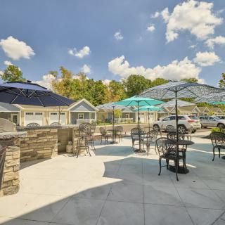 A sunny outdoor patio area with tables, chairs, and umbrellas, surrounded by stone walls and trees.