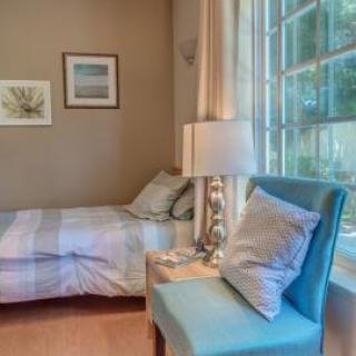 A cozy bedroom with a bed, lamp, and chair by a large window.