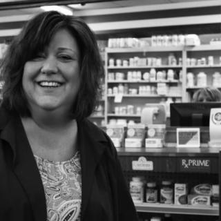 A woman smiling in a store with shelves filled with products.