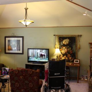 A cozy living room with a television, wheelchair, and various decor items.