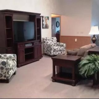 A cozy living room with patterned armchairs, a sofa, and a large TV unit.