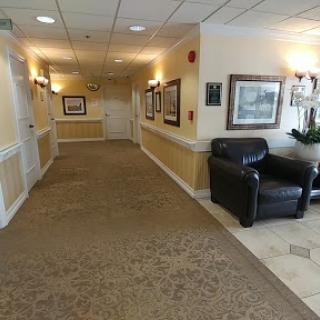A well-lit hotel hallway featuring artwork on the walls and a comfortable chair.