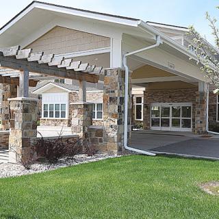 A modern building with a stone facade and a covered entrance surrounded by green grass.