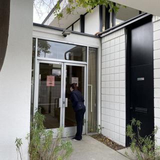 A person standing at the entrance of a modern building, looking through a glass door.