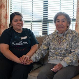 A caregiver and an elderly woman share a moment of companionship while sitting together.