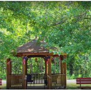 A serene park setting with a charming wooden gazebo surrounded by lush greenery and benches.