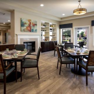 A cozy dining area featuring elegant tables and chairs, with a fireplace and artwork adding warmth to the space.