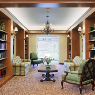 A cozy library space featuring plush seating and well-stocked bookshelves, illuminated by a decorative chandelier.