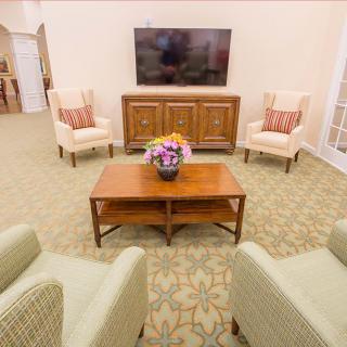 A cozy living room with comfortable seating, a large television, and a coffee table adorned with a floral arrangement.