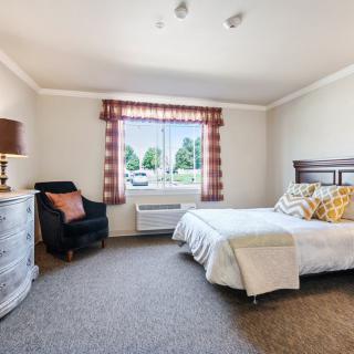 A cozy bedroom with a neatly made bed, an armchair, and a window letting in natural light.