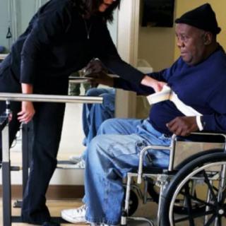 A caregiver assists an elderly person in a wheelchair during physical therapy.