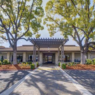 A building entrance shaded by large trees and surrounded by landscaped grounds.