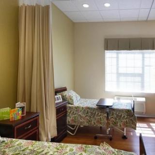 A hospital room with two beds separated by a curtain, featuring a window and a nightstand.