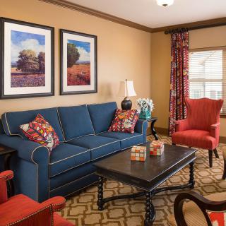 A cozy living room with a blue sofa, accented by red chairs and decorative pillows, featuring framed artwork and a stylish coffee table.