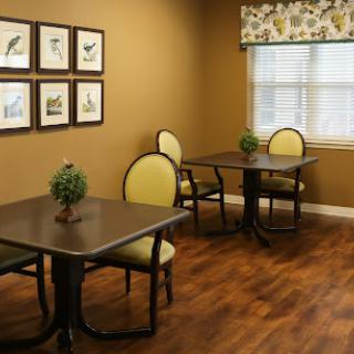 A cozy dining area featuring two tables with chairs, framed artwork on the wall, and a bright window.
