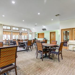 A spacious dining area with multiple tables and chairs, featuring large windows and a carpeted floor.