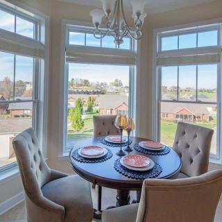 A cozy dining area with a round table set for four, surrounded by large windows that let in ample natural light.