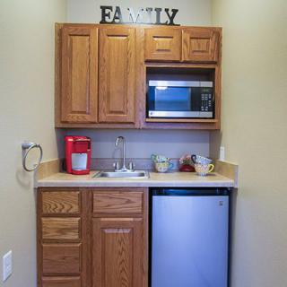 A compact kitchenette with wooden cabinets, featuring a microwave, mini fridge, sink, and coffee maker.