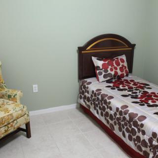 A small bedroom with a single bed and floral bedding, alongside a vintage chair and green walls.