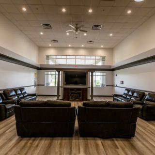 A spacious and modern living room with leather sofas arranged around a large television, featuring wood flooring and a ceiling fan.